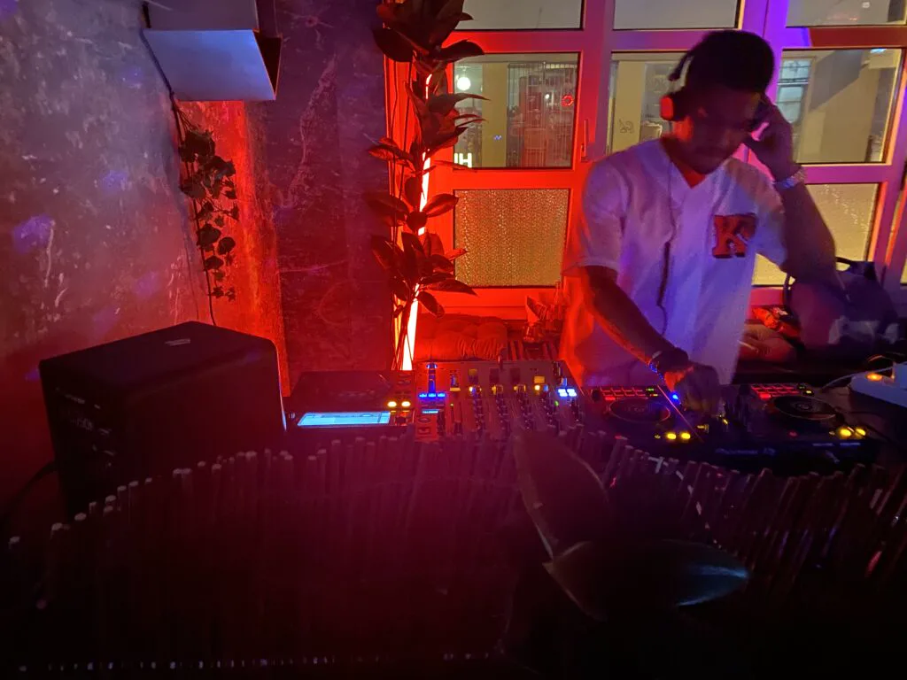 DJ Manoss mixing behind Pioneer CDJs under red club lighting